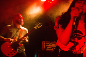Eine Frau singt in ein Mikrofon auf der Bühne, wür ein Mann Gitarre spielt.