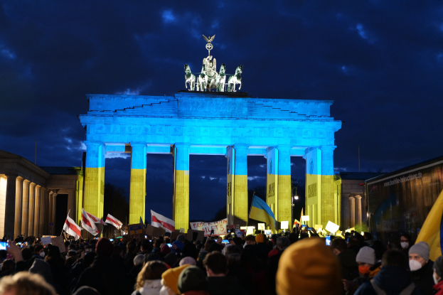 Menschenmenge mit Fahnen und Plakaten vor dem Brandenburger Tor in Berlin, mit einer Banner auf der rechten Seite.