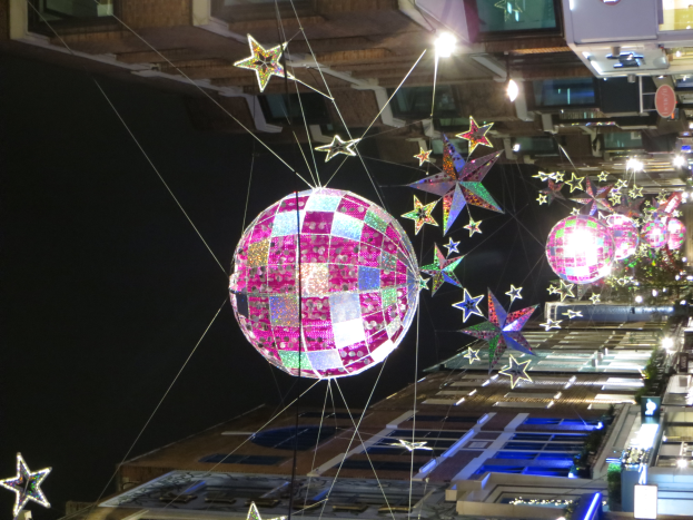 Eine Stadtstra├če bei Nacht mit zahlreichen Lichtern und D├Ącor, mit einem gro├čen Diskokugel, die von einem Geb├Ąude h├Ąngt und eine festliche Atmosph├Ąre schafft.