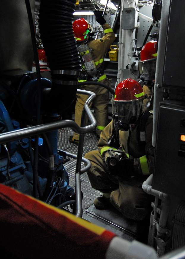Feuerwehrleute in Helmen und Schutzausrüstung an einem Löschfahrzeug mit Rohren und einer Lampe im Hintergrund.
