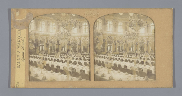 Ein altes Foto eines prächtigen Hotel-Speisesaals mit Tischen, Stühlen, Kronleuchtern und Fenstern, auf dem links ein Schild mit der Aufschrift "Sale à Manger, Grand Hotel" zu sehen ist.