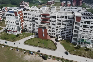 Luftaufnahme eines großen Krankenhauses mit Solarpaneelen auf dem Dach, umgeben von Bäumen, Gras, Fahrzeugen, Menschen, Strommasten und einer Tafel, die ein Solarprojekt anzeigt.