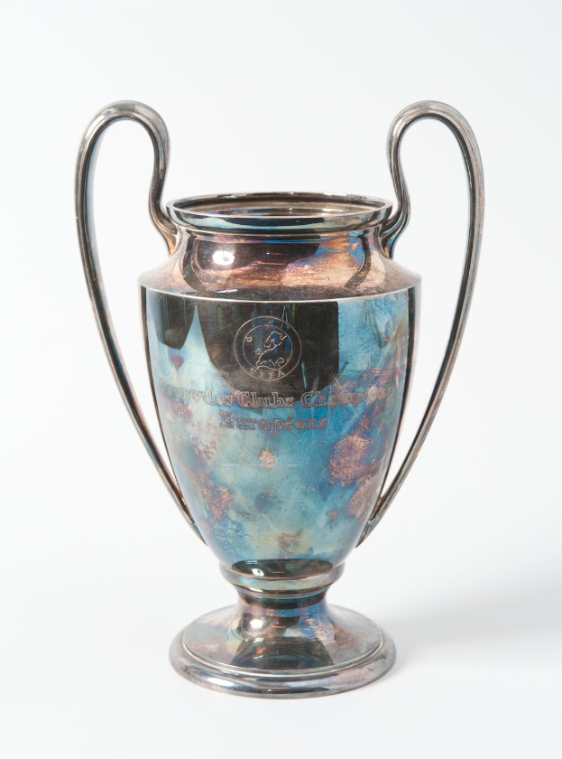 Der UEFA-Champions-League-Pokal, ein silberner und blauer Stahlbecher mit zwei Griffen, der mit "UEFA Champions League" eingraviert ist, vor einem weißen Hintergrund.