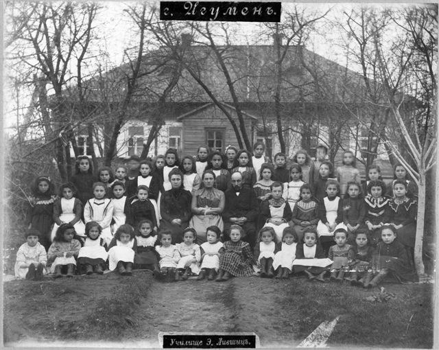 Schwarzes und weißes Foto einer Gruppe von Kindern, die vor einem Gebäude mit Fenstern posieren, umgeben von Bäumen und einem klaren Himmel, mit dem Text "Jugoslawien, die erste Schule der Welt" unten.