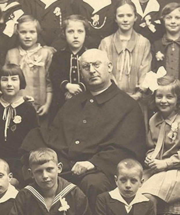 Ein altes Schwarz-Wei├č-Foto eines strengen Mannes, der in der Mitte sitzt und von einer Gruppe bewundernder Kinder umgeben ist.