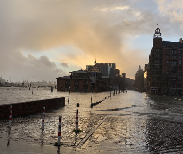 Überschwemmte Straße in Hamburg, Deutschland, mit Wasser, das die Straße, Pfähle, Schilder, Gebäude und eine Brücke bedeckt.