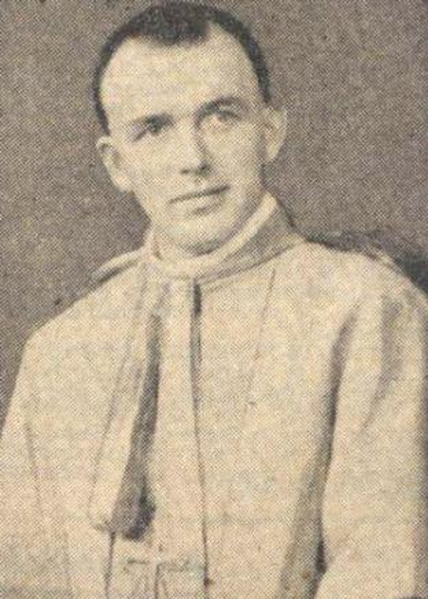 Ein Schwarz-Weiß-Foto eines Mannes in Priesterrobe, der eine weiße Robe mit schwarzem Kragen und Manschetten und eine schwarze Mütze mit einer weißen Feder trägt, mit gefalteten Händen und ernster Miene.