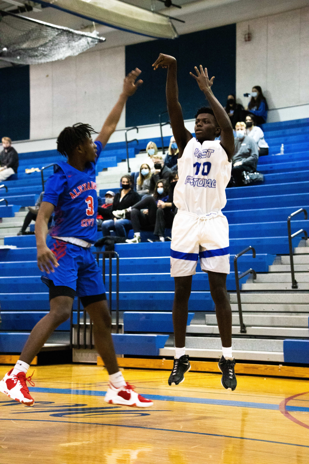 Zwei Männer spielen Basketball auf einem Court mit Zuschauern, Menschen sitzen auf Treppen im Hintergrund und eine Decke mit Lampen und Netz oben.