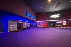 Innenseite eines Kinos mit lila Teppich, Text und Bildschirme an den Wänden und Deckenleuchten.