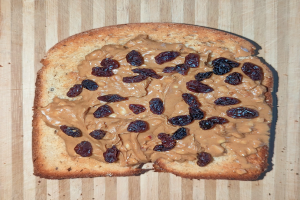 Stück Brot mit Erdnussbutter und Rosinen auf einer hölzernen Oberfläche.