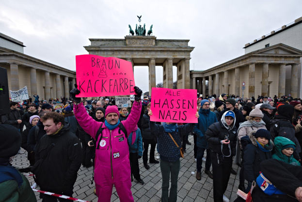 Gruppe von Menschen protestiert vor dem Brandenburger Tor in Berlin, hält Schilder gegen die Anti-Nazis-Bewegung der deutschen Regierung, mit Gebäuden und Statuen im Hintergrund unter einem klaren blauen Himmel.