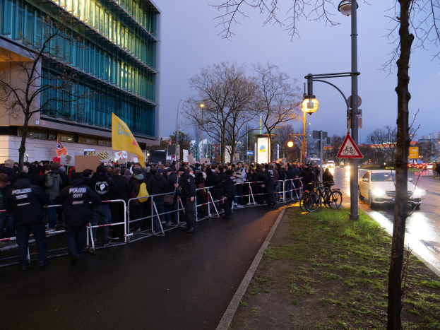 Eine große Gruppe von Menschen steht vor einem Gebäude während einer Demonstration in Berlin, mit Schildern, Barrikaden und Fahrrädern in der Nähe.