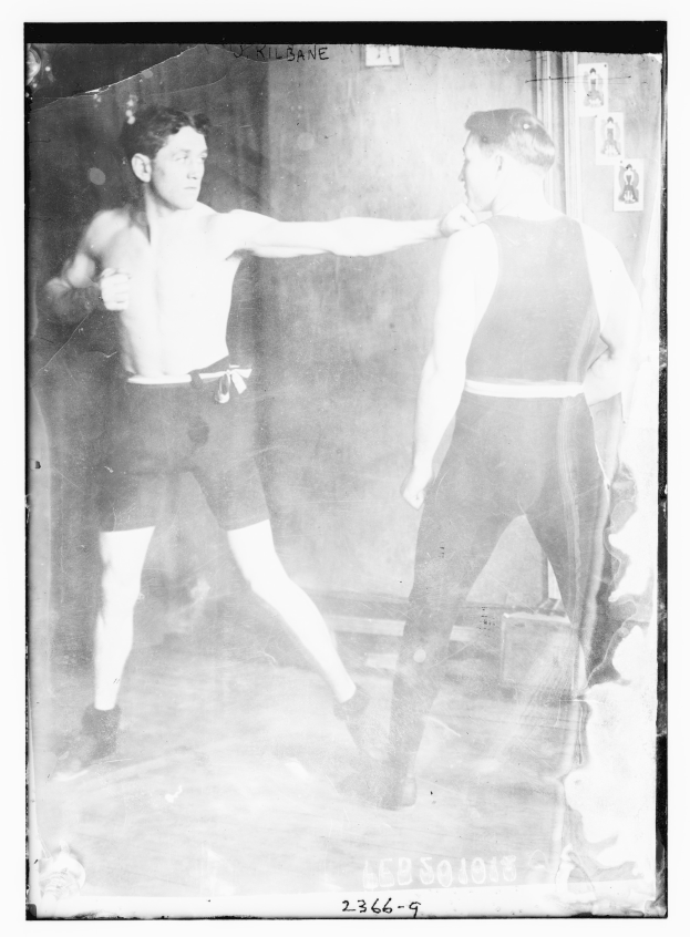 Schwarzes und weißes Foto von zwei Boxern in einem Ring mit Postern an der Hintergrundwand und Text unten.