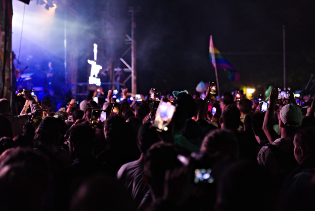 Eine Menge Menschen bei einem Konzert hält ihre beleuchteten Handys hoch, während auf der Bühne Instrumente gespielt werden.