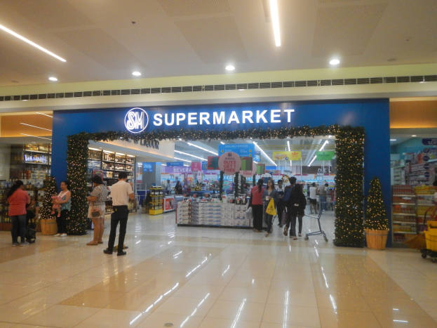 Gruppe von Menschen vor einem Supermarkt mit Einkaufstaschen, Einkaufswagen, Topfpflanze, Regalen, Schildern und Deckenbeleuchtung.