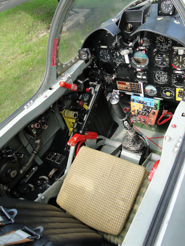 Ein kleines Flugzeugcockpit mit einem Sitz, Geschwindigkeitsmesser und anderen Gegenständen, das eine Straße und Gras außerhalb der Glasfenster zeigt.
