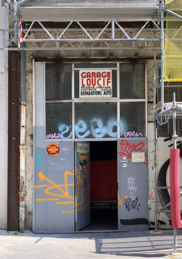 Ein Gebäude mit Graffiti, einer Tür, einer Texttafel, Metallstangen, einem Rohr, einem gelben Tuch und einer Straße unten.