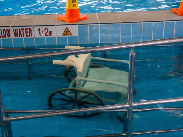 Ein Schwimmbad mit einem Stuhl in der Mitte, umgeben von Sicherheitstonnen und einem Geländer, und ein Schild an der Wand, das verfügbare Schwimmausrüstung anzeigt.