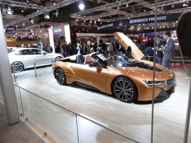 Ein elegantes schwarzes BMW i8 Cabrio mit Chromakzenten auf der Frankfurter Motor Show umgeben von formell gekleideten Gästen in einer Atmosphäre der Aufregung.