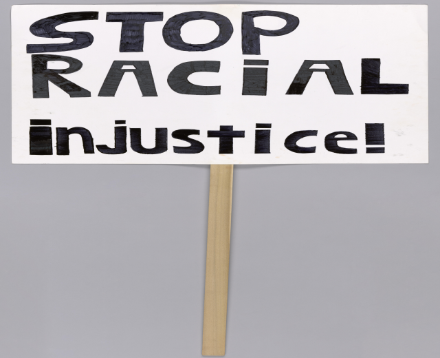 Ein weißes Schild mit schwarzer Schrift, die 'Stop Racial Injustice' lautet.