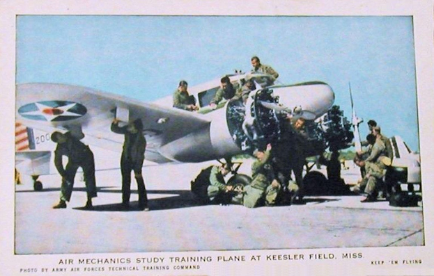 Eine Gruppe von Menschen um ein Flugzeug auf einer Landebahn herumstehend mit einem klaren blauen Himmel im Hintergrund und Text unten lesend "Luftmechanik-Studium Training Flugzeug auf Keesler Field, Miss."