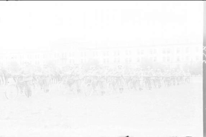 Schwarzes und weißes Foto von Radrennfahrern im Schnee an einem Gebäude vorbei.