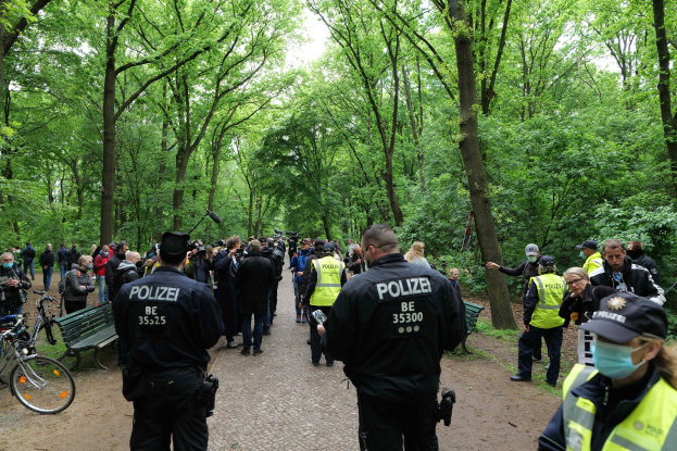 Gruppe von Polizeibeamten vor einer Menge bei einer Anti-Terror-Demonstration in Berlin, mit Fahrrädern und einer Bank im Vordergrund und Bäumen im Hintergrund.