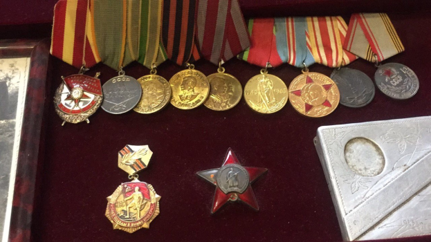 Eine hölzerne Schachtel mit verschiedenen Medaillen, darunter ein roter Stern als Symbol der Sowjetunion, ordentlich angeordnet mit einem Objekt auf der rechten Seite.