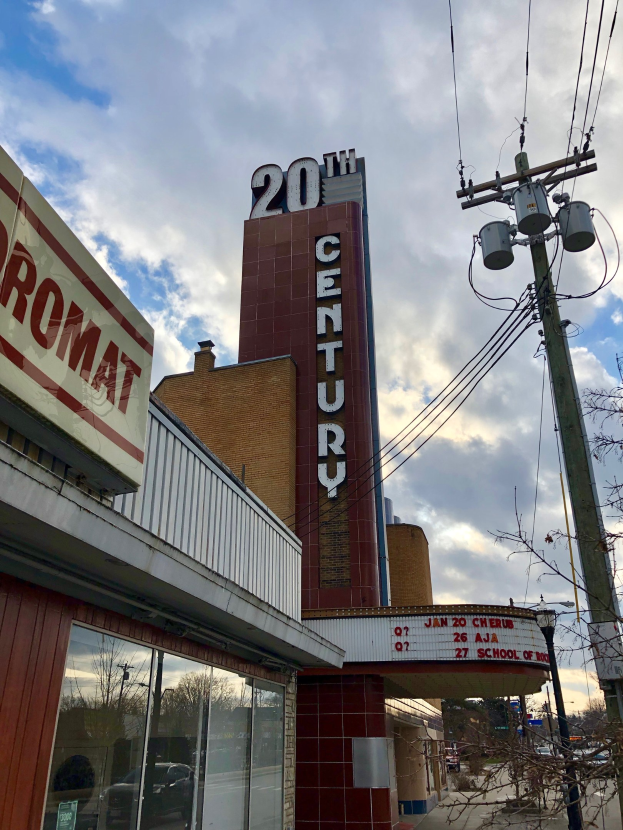 Außenansicht des 20. Jahrhundert Theaters in Detroit, Michigan, mit Glaswänden, Namensschildern, umgeben von Bäumen und Strommasten mit Drähten vor einem bewölkten Himmel.