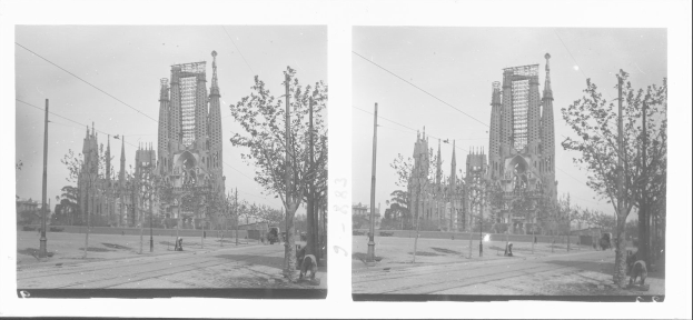 Schwarz-weiß-Foto einer Stadtstraße mit einer Kirche im Hintergrund, umgeben von Bäumen, Pfählen und Menschen, wobei die Kirchenfassade restauriert wird.