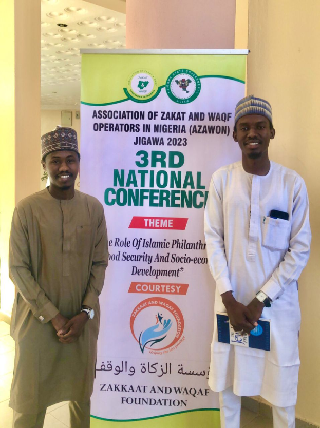 Zwei Männer vor einem Banner mit der Aufschrift "3. Nationale Konferenz" mit einer Säule und Deckenbeleuchtung im Hintergrund, wahrscheinlich an der 2023er-Veranstaltung teilnehmend.