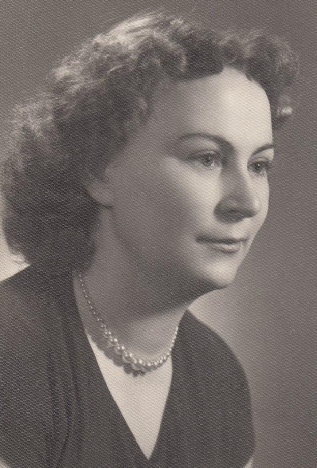 Ein Schwarz-Weiß-Foto einer Frau mit ernstem Gesichtsausdruck, die eine Kette trägt und ein einfaches Kleid mit hohem Kragen und langen Ärmeln trägt, ihre Haare zurückgekämmt und ihre Augen konzentriert.