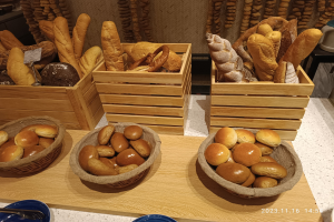 Ein Holztisch zeigt Körbe mit verschiedenen Brotsorten, Teller und Löffel in einer Pariser Bäckerei mit einer gewässerten Wand im Hintergrund.