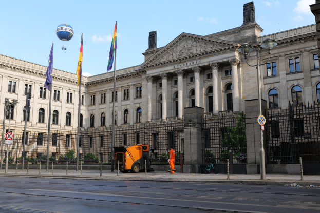 Großes modernes Gebäude mit vielen Fenstern, identifiziert als der Bundestag in Berlin, Deutschland, umgeben von Straßeninfrastruktur, Fußgängern und Fahnen, unter einem bewölkten Himmel.