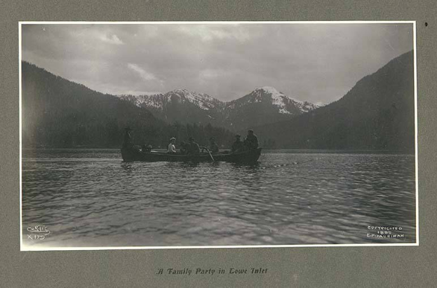 Schwarz-weiß-Foto einer Familie in einem Kanu auf einem See mit Bergen und Bäumen im Hintergrund, Himmel oben sichtbar, Text unten.