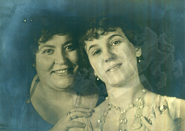 Zwei Frauen lächeln warm in einem alten Foto, ihre strahlenden Augen spiegeln lebhafte Ausdrücke.