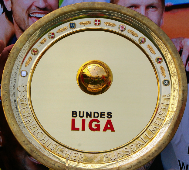 Goldener Schild mit "Bundesliga"-Text, gehalten von einem Mann mit einem Banner im Hintergrund, das drei Personen zeigt.