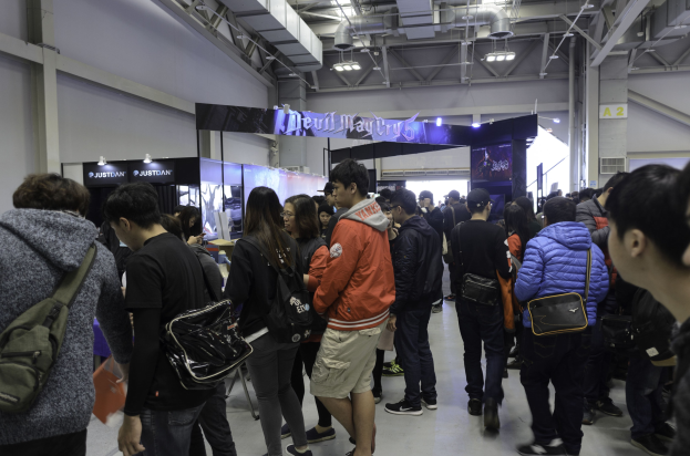 Menschen vor einer Menge auf einer Gaming-Messe, mit Schildern, Lichtern und Deckenrohren im Hintergrund.