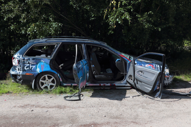 Auto krachte in die Straßenrandwiese mit Bäumen im Hintergrund.