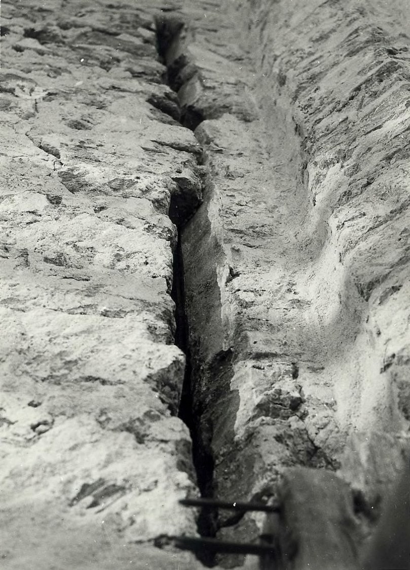 Schwarzes und weißes Foto einer große Riss im Boden, wahrscheinlich ein Entwässerungskanal, mit einem sichtbaren Wasserzeichen auf der linken Seite.