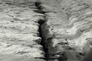 Schwarzes und weißes Foto einer große Riss im Boden, wahrscheinlich ein Entwässerungskanal, mit einem sichtbaren Wasserzeichen auf der linken Seite.