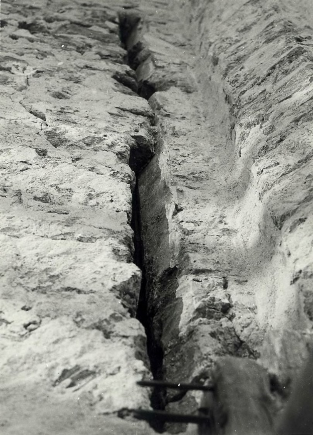 Schwarzes und weißes Foto einer große Riss im Boden, wahrscheinlich ein Entwässerungskanal, mit einem sichtbaren Wasserzeichen auf der linken Seite.